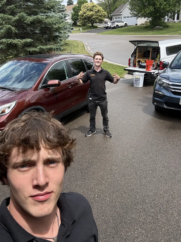 Mobile detailer working beside a truck rig loaded with equipment in a residential driveway